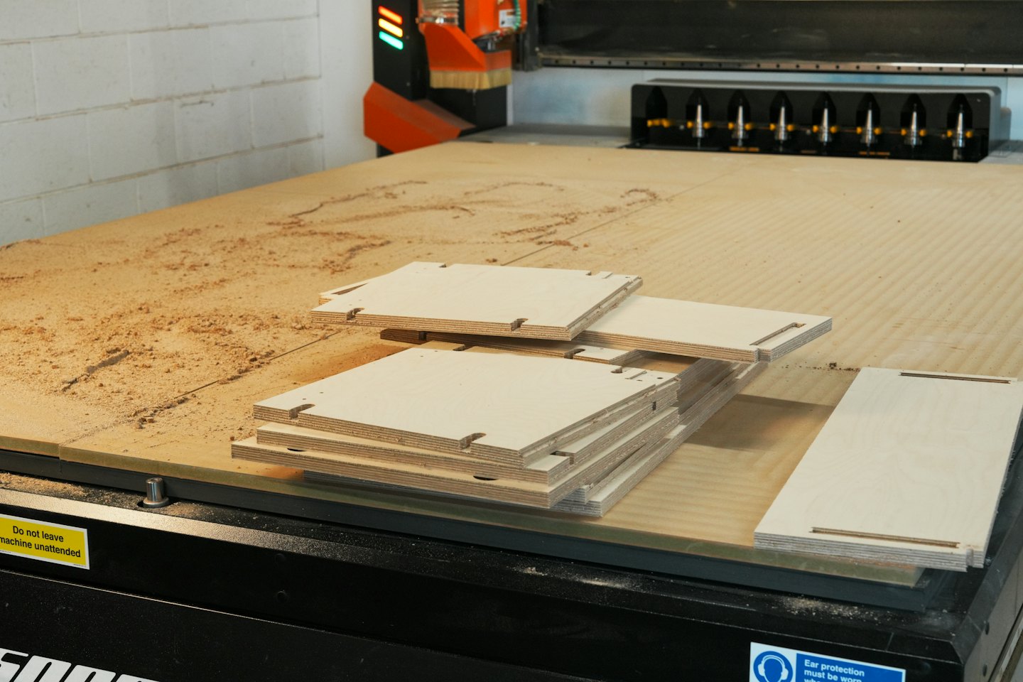 CNC router cutting plywood in a workshop with wood dust.